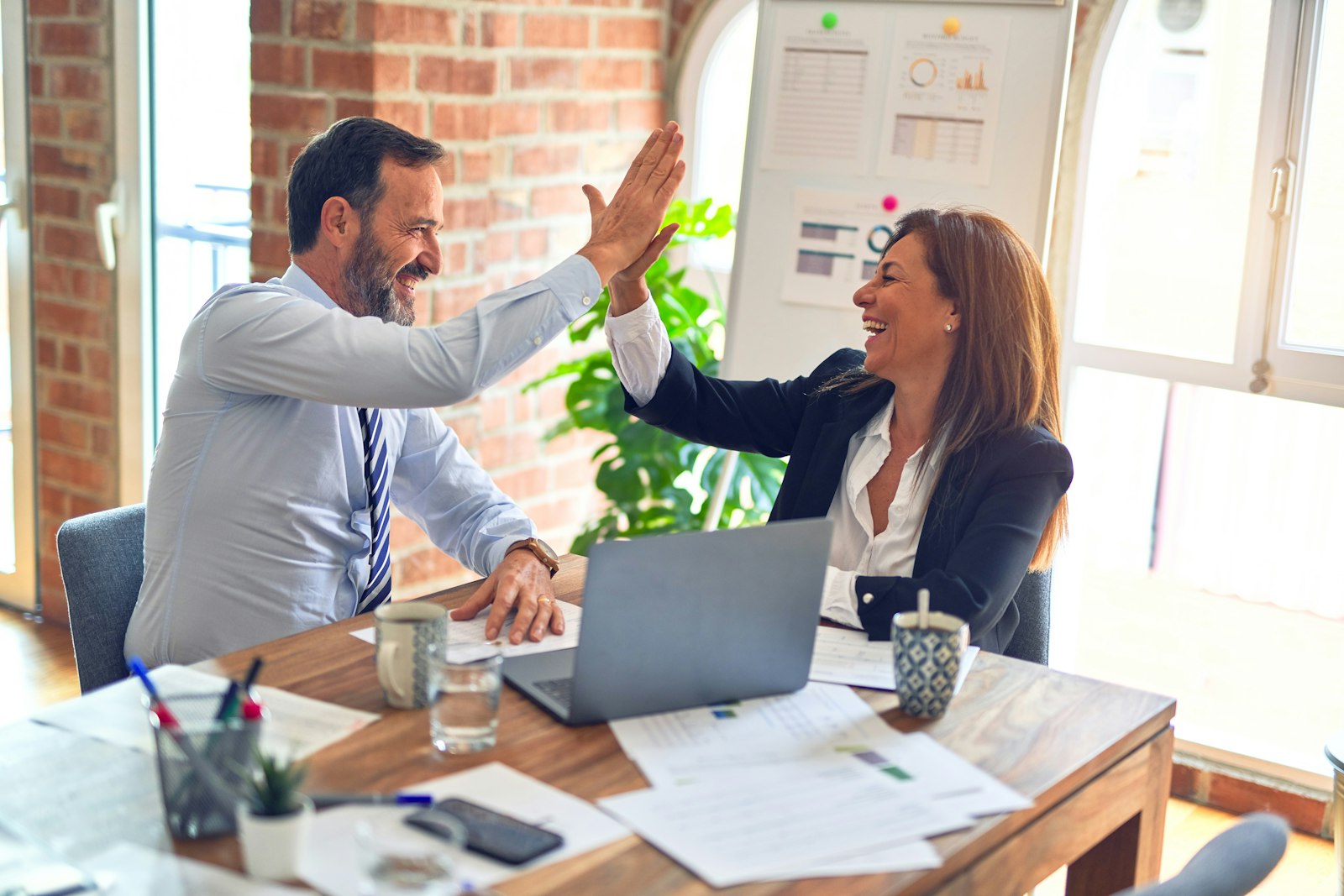 Two colleagues celebrating at a desk with a laptop in a bright office